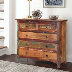 an old dresser with wooden drawers in a living room next to stairs and a painting on the wall