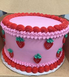 a pink cake with red icing and strawberries on top is in a box