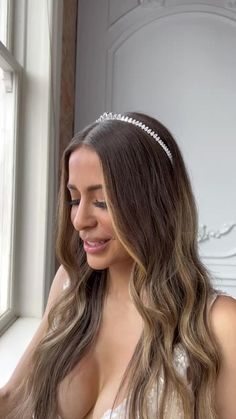 a woman with long hair wearing a tiara looking out a window at the camera