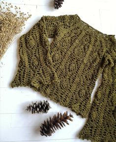 a knitted sweater with pine cones on the floor next to it and some dried plants