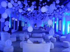 a room filled with white couches and balloons hanging from the ceiling above it is lit up by blue lights