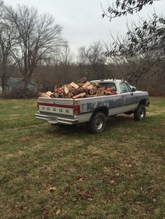 an old pickup truck loaded with wood sitting in the grass next to a tree filled field