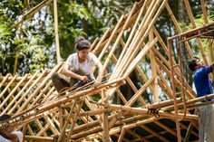 two men are building a house out of bamboo sticks in the forest, while another man looks on