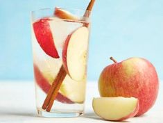 an apple and cinnamon stick in a glass of ice water with apples on the side