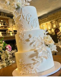 a white wedding cake with flowers on the top and initials on the side is sitting on a table