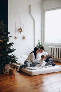 a man and woman sitting on top of a bed next to a small child in front of a christmas tree