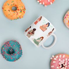 various donuts and doughnuts are scattered around a coffee mug on a blue surface