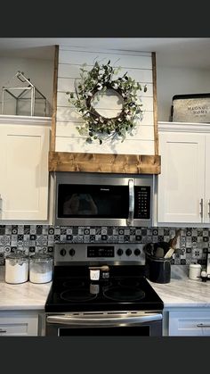 a kitchen with a wreath on the wall above an oven and stove top, surrounded by white cabinets