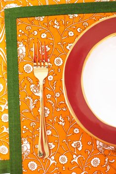 an orange and white place setting with silverware on it, along with a green border