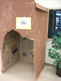 an open cardboard box with writing on it and a potted plant in the corner