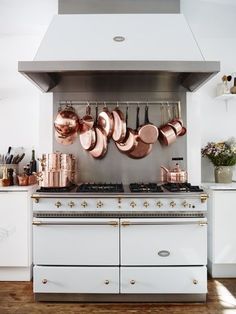 copper pots and pans are hanging on the wall above an oven in this kitchen