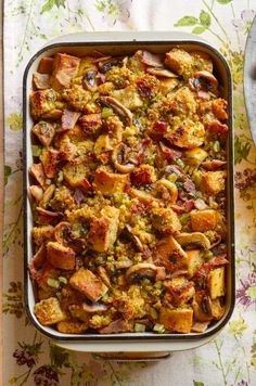 a casserole dish filled with stuffing and vegetables on a floral table cloth next to a spoon