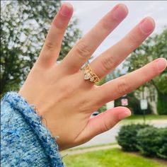 a person's hand with a ring on it in front of some bushes and trees