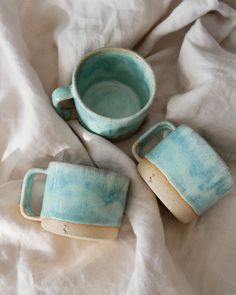 three ceramic cups sitting on top of a bed