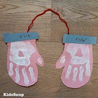 two pink handprinted mitts are hanging on a wooden floor with red string