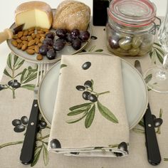 a table topped with plates filled with food next to wine glasses and cheese board covered in olives