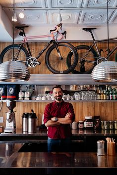 a man standing in front of a bar with two bikes hanging from the ceiling above him