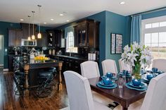 a kitchen and dining room with blue walls, hardwood floors and white chairs in it