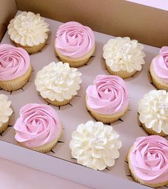 twelve cupcakes in a box with pink frosting and white flowers on top