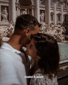 a man and woman standing next to each other in front of a fountain