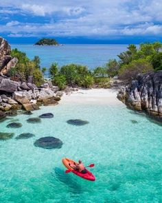 a man in a red kayak is floating on the water near some rocks and trees