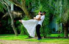 a man carrying a woman on his back in front of some trees and grass with palm trees behind them