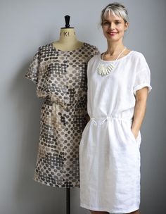 a woman standing next to a mannequin wearing a white dress with black dots