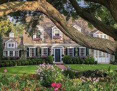 a large house surrounded by lush green grass and trees with flowers in front of it