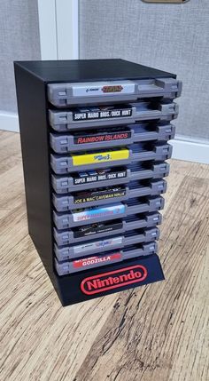 a stack of nintendo games sitting on top of a wooden floor next to a wall