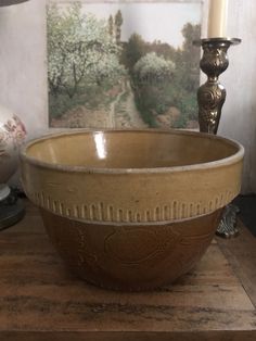 a brown bowl sitting on top of a wooden table next to a candle and painting