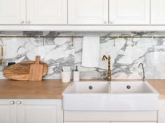 a kitchen with marble counter tops and white cabinets, gold faucets and wooden cutting board