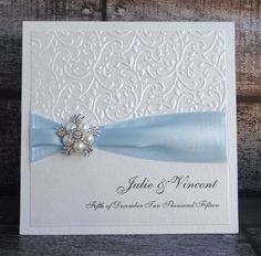 a white wedding card with blue ribbon and brooch