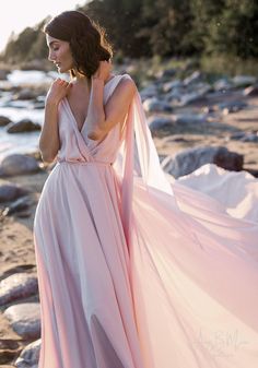 a woman in a long pink dress standing on the beach with her back to the camera