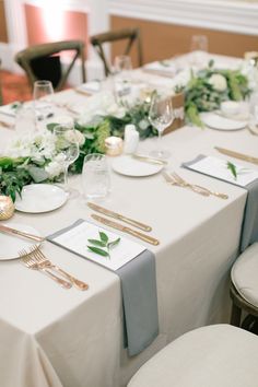 the table is set with white and green flowers, silverware, and place settings