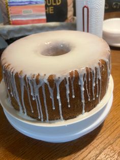 a bundt cake with icing on a white plate sitting on a wooden table