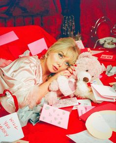 a woman laying on top of a bed holding a teddy bear next to a pile of cards