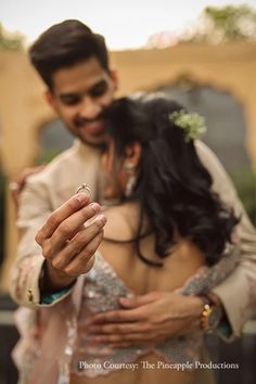 a bride and groom holding their wedding ring in front of the camera, while they stand close to each other