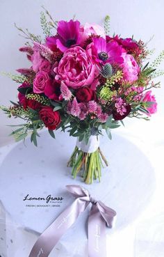 a bouquet of pink and red flowers sitting on top of a white table with a ribbon