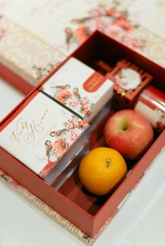 an orange and some apples in a red box on a white tableclothed surface