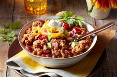 a bowl filled with chili, cheese and other toppings on top of a wooden table