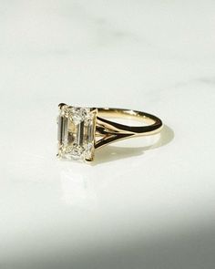 a yellow gold engagement ring with an emerald cut diamond in the center, on a white background