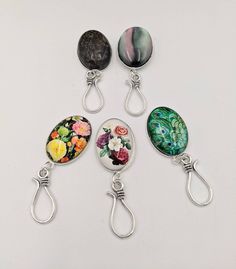 four different types of glass cabochons with flowers and peacocks on them, hanging from metal hooks