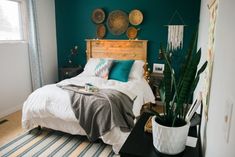 a bedroom decorated in teal and gold with a bed, potted houseplant, and decorative wall hangings