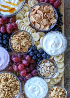 an assortment of snacks are arranged on a wooden platter with grapes, crackers and yogurt