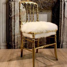 a gold chair with a white fur seat pad on it in front of a fireplace