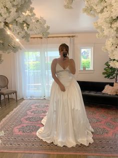 a woman in a wedding dress taking a selfie with her cell phone while standing on a rug