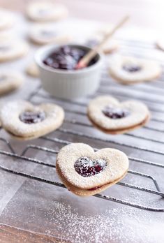 heart shaped cookies sitting on top of a cooling rack next to a bowl of jelly