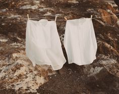 two white shirts hanging on a clothes line next to some rocks and water in the background