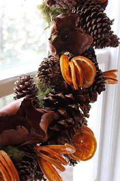 an arrangement of pine cones and oranges hanging from a window sill