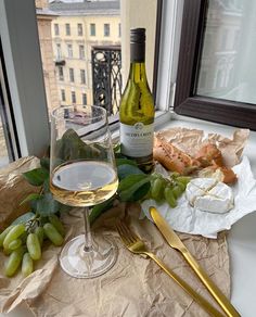 a glass of wine, cheese and grapes on a table with a window in the background